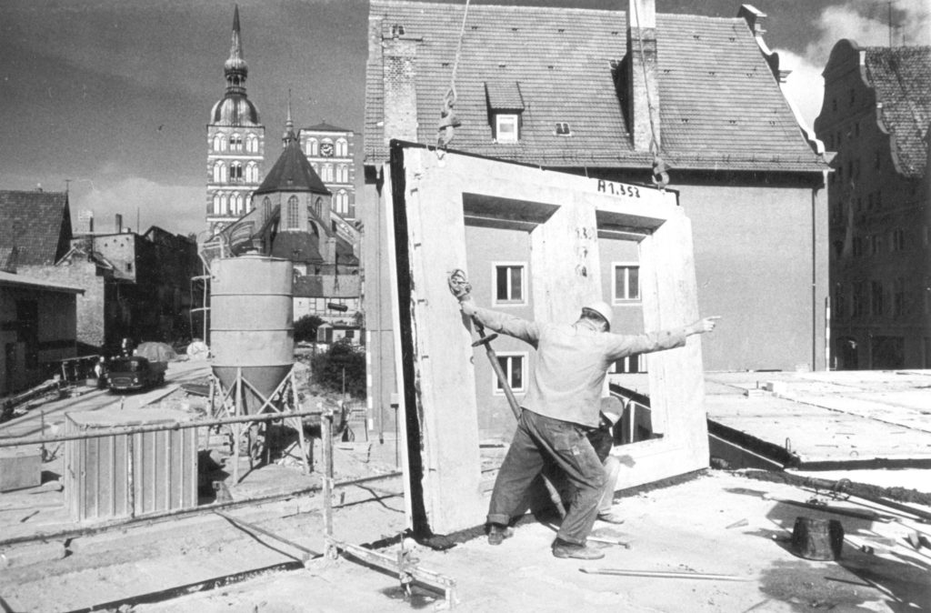 Ein Bauarbeiter platziert ein Plattenbauelement im Bebauungsgebiet Badenstraße. Im Hintergrund sind die Türme der Nikolaikirche zu sehen.